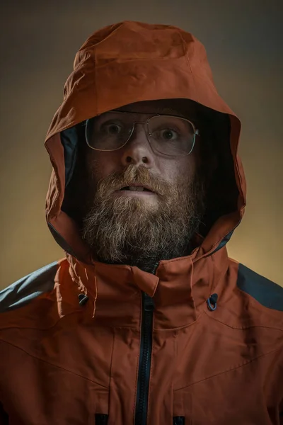 Scary bearded man in orange jacket or trench coat. Rapist or geeky nerdy hipster look. Nerdy glasses on a scary man in a jacket with hoodie or hood.