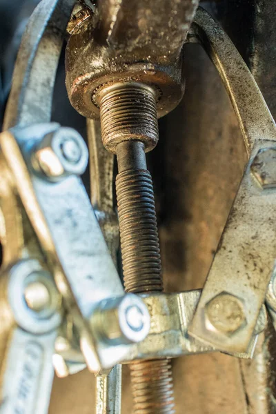 Three jaws puller in action while removing a metal arm from a splined metal axle to renew bearings and seals. Stubborn seized metal part being pulled out with jaws puller.