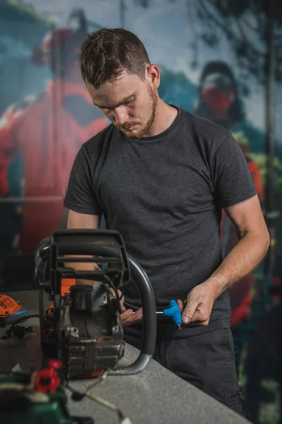 Profesyonel tamirci vidayı gevşetmek için anahtarla elektrikli testereyi tamir ediyor. Süslü bir atölyede testere tamir eden adam.