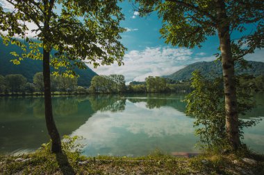 Soca nehrinin sakin gölü Most na Soci 'de sabahın erken saatlerinde. Ağaçların arasından eğlence amaçlı kanoya doğru bak.