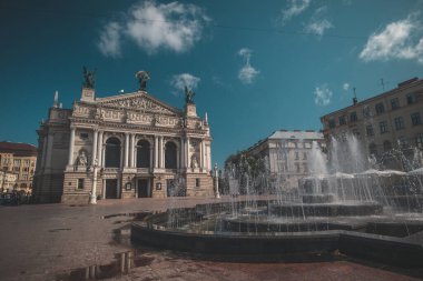 Sıcak bir yaz gününde Ukrayna, Lviv 'de güzel bir opera binası. Mavi gökyüzünde bazı bulutlar görüldü. Ön planda çeşme görülür..