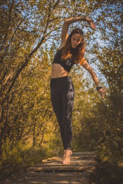 Şirin esmer beyaz kadın ya da kız güzel bir sonbahar ormanında eski ahşap bir köprüde otururken yoga yapıyor. Doğada huzur ve sükunet.