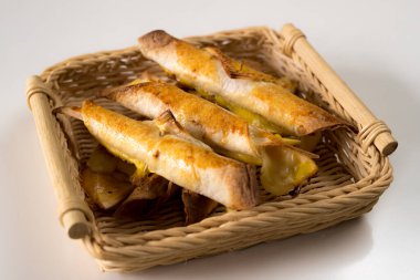 Hasır sepette servis edilen beyaz izole edilmiş bir arka planda taze pişmiş taquitos yığını. Lezzetli Meksika atıştırmalıkları fırından yeni çıktı. Yan görünüm