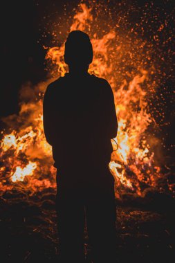 Büyük bir şenlik ateşinin önünde duran bir adamın silueti. Cesur ve ateşli bir ifade. Büyük bir ateşin önünde gururlu bir adam duruyor.