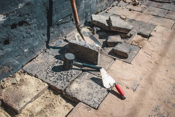 View of construction works on a sidewalk . tile or granite blocks on a pedestrian path on a street. Visible open floor with hammer, sand and other tools around