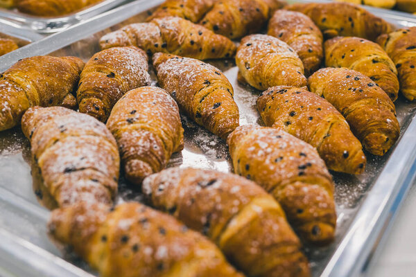 Batch of croissants stacked on a silver plate at a gala event or party. Sweet pastry products on display, covered with chocolate chips and sugar.
