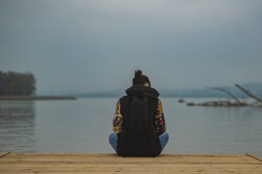 İskelenin ucunda tek başına oturan genç bir kadın. Sonbaharda bulutlu sıkıcı bir gün, dinlenen bir kızla soğuk bir ortam..