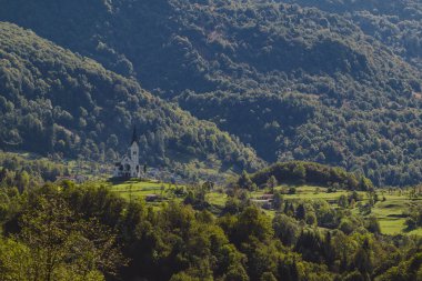 Bulutlu ve güneşli bir sonbahar gününde Kobarid 'e yakın Dreznica köyündeki güzel İsa' nın Kalbi Kilisesi. Çayırların arasında yükselen kilise