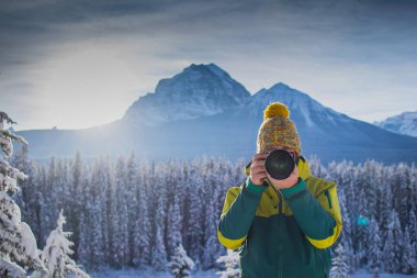 Bir adam güzel karlı dağ manzarasını çekiyor. Kışlık giysiler ve telefoto mercekli bir adam güzel bir dağ manzarasının fotoğraflarını çekiyor. Önden görüntü.