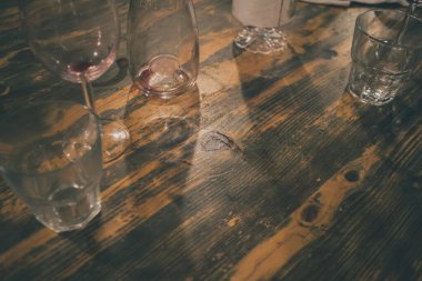 Büyük ahşap bir masada farklı bardaklar, görünür şarap kalıntıları.