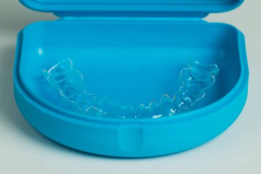 Beyaz üzerine izole edilmiş mavi bir çantada şeffaf plastikten yapılmış ortodontik diş teli. Dişleri hizalamak için kullanıcı.