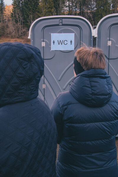 Waiting in a long line or queue for a portable toilet or portapotty at an event.