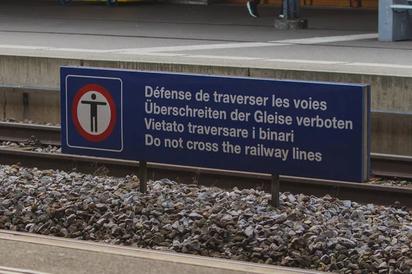 Sign board for preventing people crossing the railroad tracks, white writing on blue board with writings in different european languages.