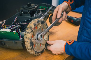 Çim biçme makinesinin tekerleklerini söküp çıkaran bir servis elemanı, çamurda ve çimlerde bir yıl kullanıldıktan sonra motorlu çim biçme makinesinin bakımını yapan bir servis elemanı. Robot çim biçme makinesinin düzenli bakımı