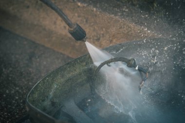 Hizmet planının bir parçası olarak yüksek basınçlı bir jet temizleyicisinin yardımıyla otonom bir çim biçme makinesinin altını temizleyen adam. Gunk dışarı uçuyor.