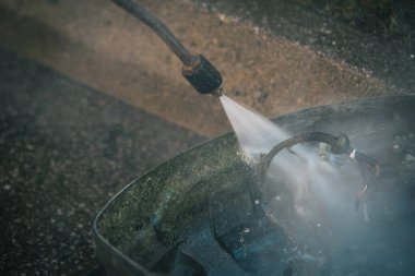 Hizmet planının bir parçası olarak yüksek basınçlı bir jet temizleyicisinin yardımıyla otonom bir çim biçme makinesinin altını temizleyen adam. Gunk dışarı uçuyor.