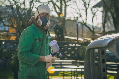 Otomotiv sprey tabancalı bir adam, antika bir arabanın restorasyonu sırasında bahçede iş üstünde. Çıplak metale ilk taban boya katmanı uygulanıyor..