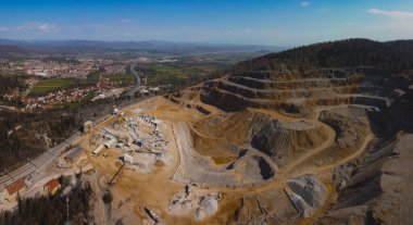 Slovenya 'nın Verd kentinde güneşli bir günde açık bir mayının ya da taş ocağının insansız hava aracı panoraması. Görülebilir teraslar ve engin kum ve taş yüzeyi. Arka planda bir şehir var..