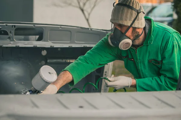 白人男性は修復プロジェクトとしてヴィンテージカーに圧縮空気塗料銃で色を噴霧しています マスクや手袋などの保護具を身に着けている男 プロの自動車画家 — ストック写真