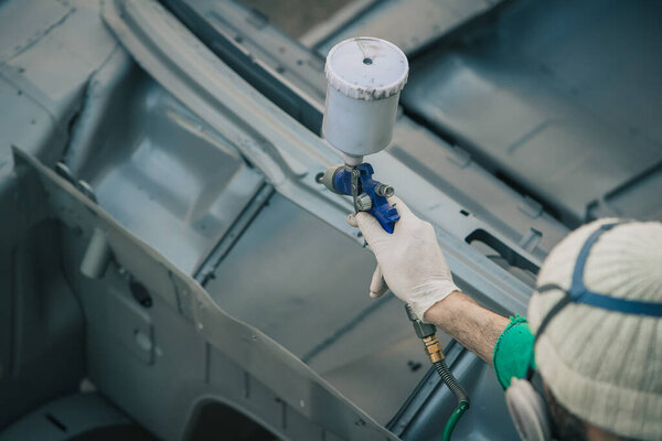 Man with automotive air spray gun in action during the restoration of a vintage car. Applying first base layer of paint onto bare metal.