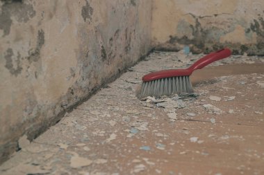 Kırmızı plastik süpürge, eski, ıslak bir yosunlu duvardan lamine zemine düşen enkazı süpürüyor. Arkasında görünen temiz yol.