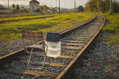 Kişisel izolasyon, indutial bir alanda video çağrısı. Dizüstü bilgisayar ve sandalye doğada ya da gün batımında tren raylarında video konferansı için kullanılıyor.