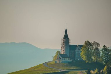 Slovenya 'nın Crni Vrh kentindeki küçük pitoresk kilise, sabahın erken saatlerinde gün doğumunda. Çan kulesi daha yeni yenileniyor. Etrafında metal iskeleler var..