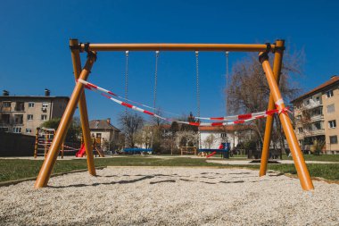 Corona virüsü kısıtlamalarından dolayı kapalı çocuk parkı ya da zincir üzerinde sallanma. Çocuklar üzerinde bürokrasi ve beyaz şerit sallanıyor.