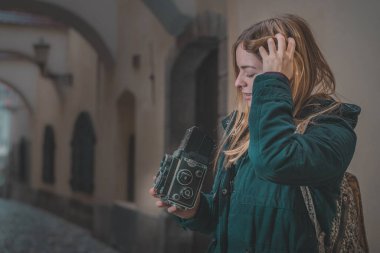 Sevimli genç sarışın, eski bir fotoğraf makinesini nasıl kullanacağını bilmediği için kafasını kaşıyor..