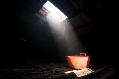 Tavan arasında sisli bir ortamda duran eski püskü kırmızı bir kova. Çatı katındaki pencereden gelen bir ışık tarafından yakılan kırmızı kova..