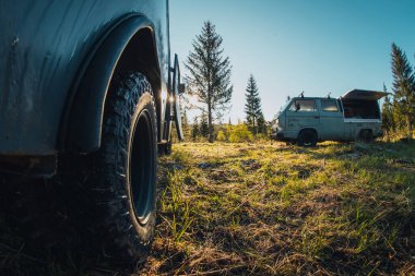 Sabah saatlerinde orman ovasında park etmiş iki eski geleneksel off-road karavanı. Ciddi bir off-road lastiği manzarası..