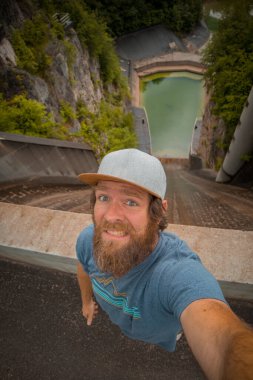 Hippi adam Slovenya 'nın Moste kentindeki hidroelektrik santrali için küçük ama dik bir barajdan selfie çekmekten korkuyor. Yukarıdan hidroelektrik barajının görüntüsü, doğrudan aşağıya bakıyor..