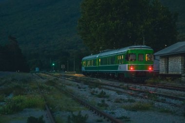 Eski tarz dizel çoklu DMU treni beyaz ve yeşil renkli geceleri kentsel olmayan çevrede. Eski bir istasyonun önünde tren..