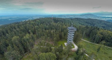 Aussichtsturm Lichtenberg, Avusturya Attergau bölgesinde metal ve ahşaptan bir kule yapan bir adam, bulutlu havada yerel tepelerin üzerinde yükseliyor..