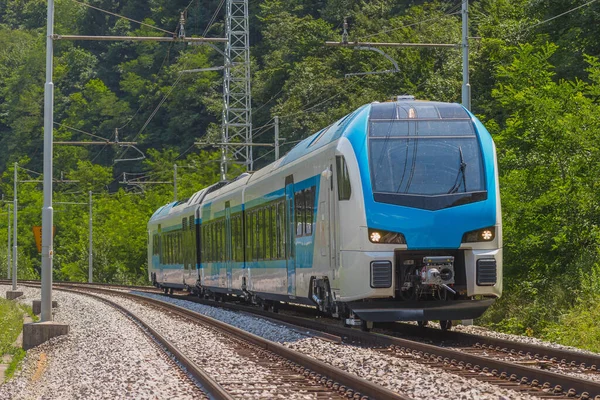 Modern and new passenger swiss made Train in white and blue color is traveling on a dual track railway line in the rural setting on a sunny hot day.