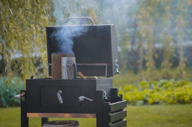 Smoker grill in a home backyard is being fired up. Container with wood and coal on a grill ready to be inserted into oven. clipart