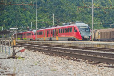 Bir banliyö istasyonunda modern elektrik ünitesi treni raylarda. Güneşli bir günde banliyö ortamında şehre doğru koşan banliyö treni..