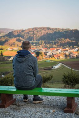 Eskiden tanıdığı köye bakarken bankta oturup dinlenen bir adamın arka görüntüsü..