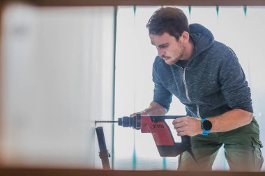 Duvarda delik açmak için elektrikli matkap kullanan bir adam. Görünür elektrikli süpürge hortumu enkazı emmek için..