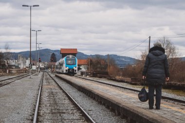Modern yolcu treni bekleyen bir yolcuyla platforma yaklaşıyor. Modern bir trenin ve yağmurlu havanın ön planında bir gezgin..