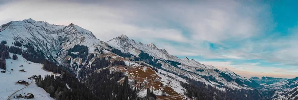 Wide aerial drone panorama of the slopes above the Adelboden and Engstligen valley, in early evening in the winter time. Some snow is visible on the majestic mountains. Looking towards Frutigen.