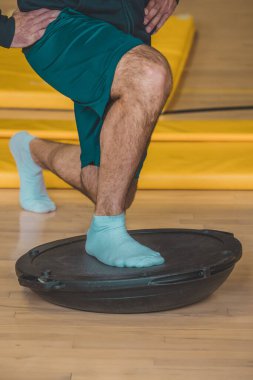 Plastik denge topu kullanan erkek antrenörün ön görüntüsü. Spor salonlarında farklı denge ekipmanları görülür..