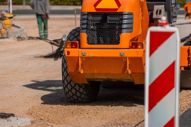 Detail of a tractor bulldozer in orange color on gravel construction site on a city street.