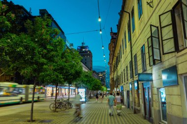 Geceleri Ljubljana 'daki Slovenya caddesinde güzel sokak ışıkları, ağaçlar, insanlar ve toplu taşıma araçları koşuşturuyor.