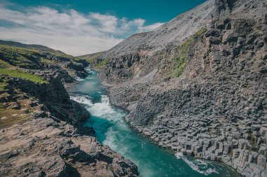 İzlanda 'daki Studlagil Kanyonu manzarası. Sıcak bir yaz gününde bazalt sütunları yüksekte duran pitoresk bir vadi. Çimenlerin arasından vurulmuş.
