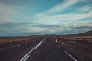 İzlanda 'daki asfalt yolun harika manzarası, dağlara doğru gidiyor. Issız dağlara doğru yol alan çizgiler ve yukarıdaki kalın bulutlar..
