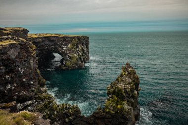 İzlanda 'nın Sfortuloft deniz feneri çevresindeki güzel manzara. Görünür kayalar, çıkıntılar, doğal kemerler ve bulutlu bir günde..