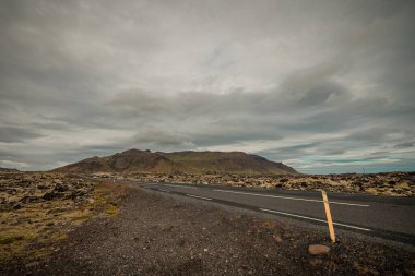 Bulutlu bir yaz gününde İzlanda yakınlarındaki Lav kayaları oluşumlarından geçen yol. Muhteşem lav tarlaları ve yol delip geçiyor..