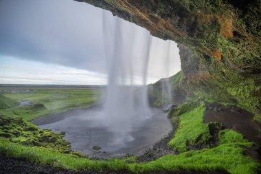 İzlanda 'da yaz sabahı Seljalandsfoss' un güzel manzarası. Şelalenin su perdesinin arkasına bak..