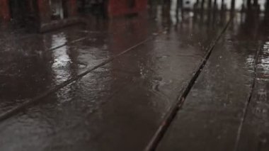 Yatıştırıcı bir yavaş çekim videosu ıslak ahşap bir güvertede yağmur damlalarını gösteriyor, dalgalanmalar ve yansımalar oluşturuyor. Yakın çekim, yağmurun sakin ritmini ve dokusunu ayrıntılı olarak yakalar..